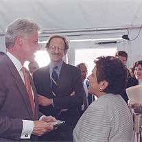 A man and woman speaking in the foreground, while another man looks on.