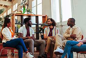 Five diverse young people having a conversation with psychologist during a group therapy session.