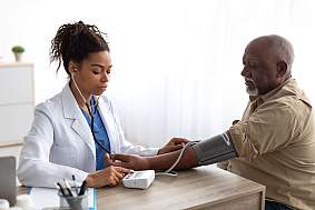 A health care professional takes a blood pressure reading from an older man