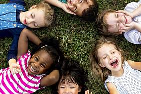 Children smiling and laughing, lying in grass in a circle formation