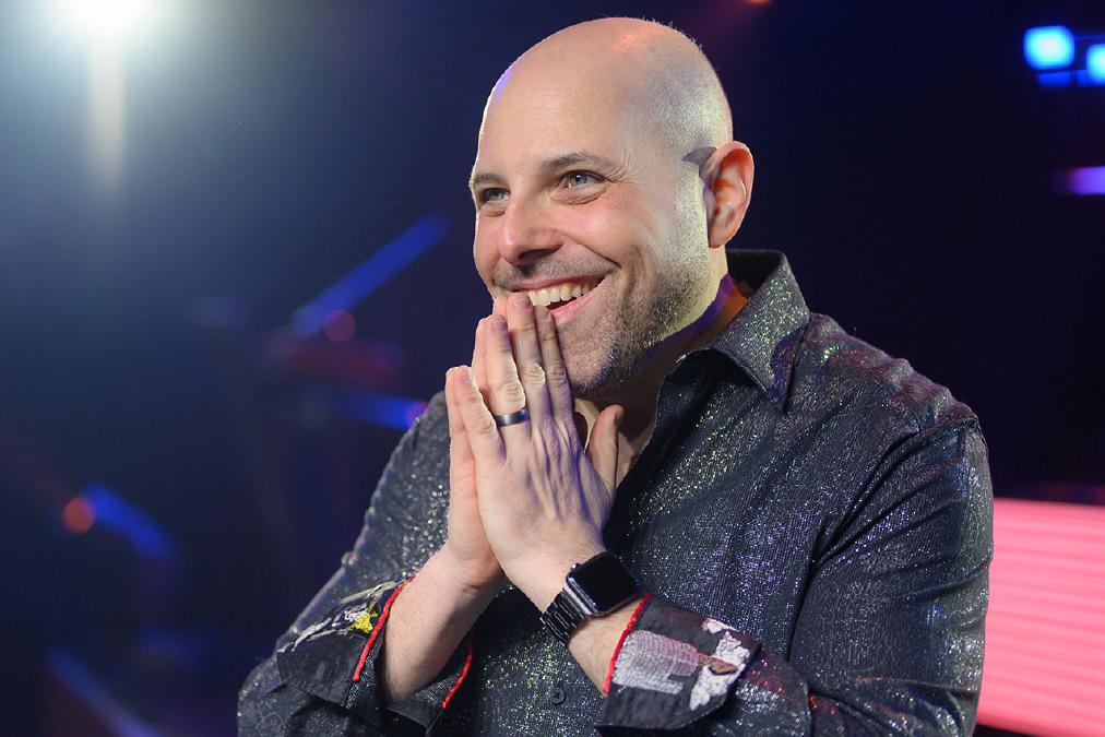 Cancer survivor stands on a stage with hands clasped together and a smile on his face