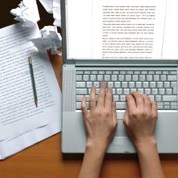 Someone writing on a laptop computer, with a printout and crumpled paper next to it