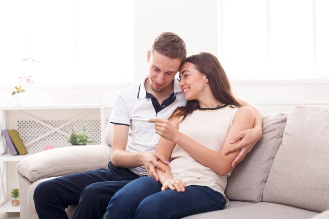 20220208-preg.jpg Young couple looking at pregnancy test on couch