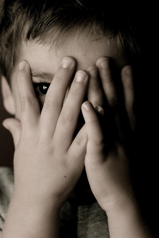 Child hiding face and looking through his fingers.