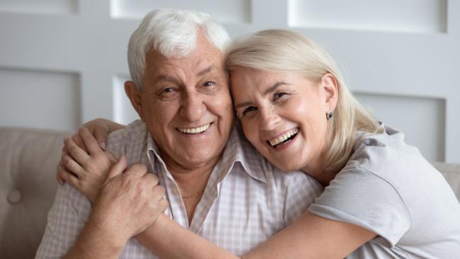 Horizontal banner happy old couple in love seated on couch embracing, laughing grey haired husband and wife pose looks at camera.
