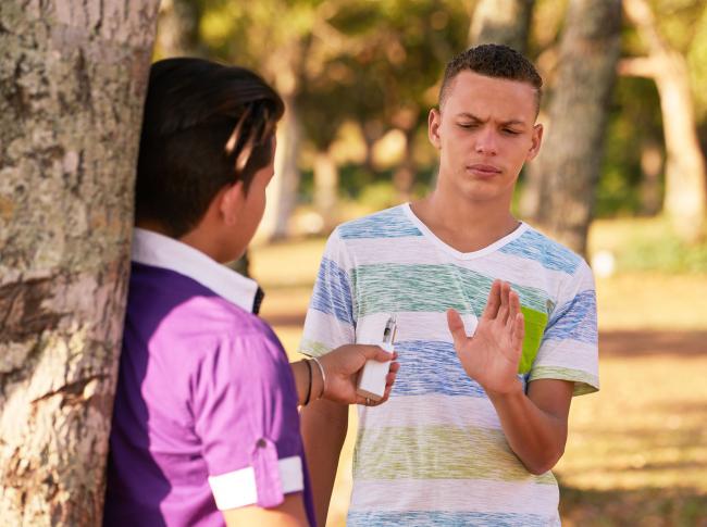 Teenager in a park turning down an electronic cigarette.