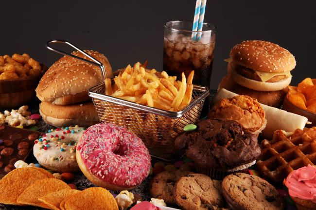 A variety of unhealthy ultra-processed foods, including donuts, potato chips, fries, waffles, and processed fish sandwich.