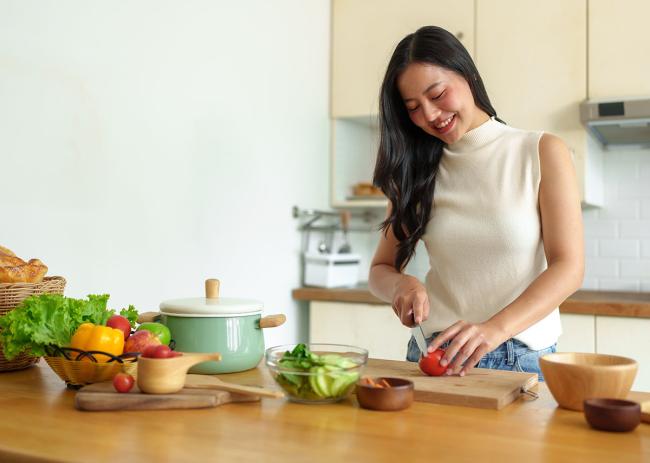Woman cutting a tomato to make a salad in the kitchen.