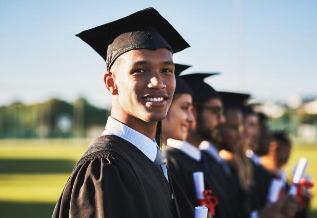 Smiling adults in graduate attire stand shoulder-to-shoulder.