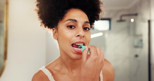 Woman using a dental floss pick in a bathroom.