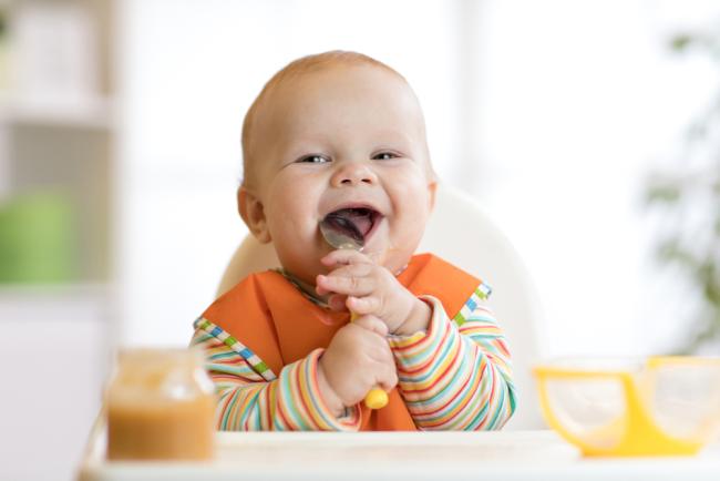 Baby smiling and putting a spoon in its mouth.