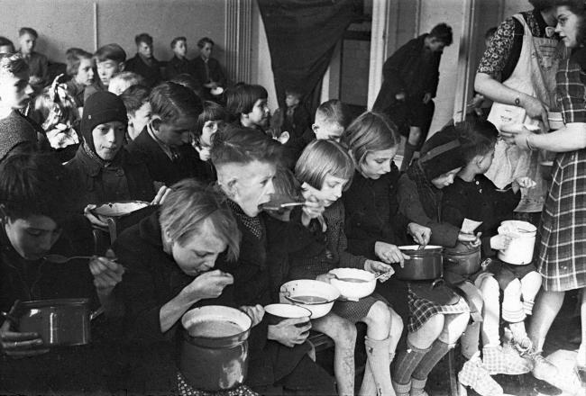 Black and white photo of a room full of Dutch children being served soup