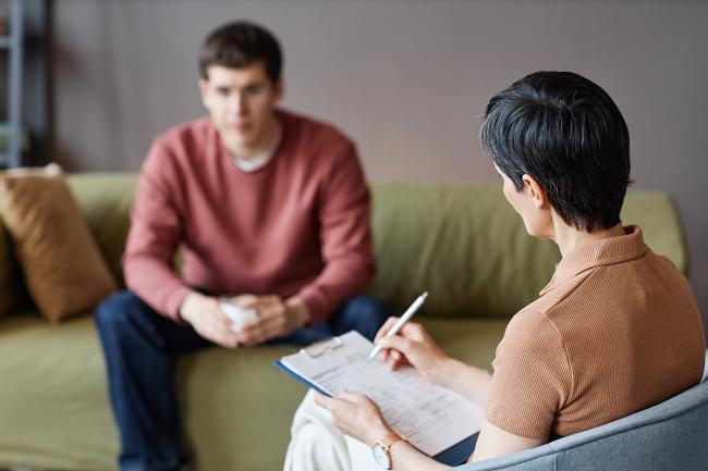 Rear view of mature therapist making notes during a conversation with a patient.
