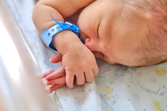 A newborn baby with a maternity hospital bracelet sleeping in a clinic crib.