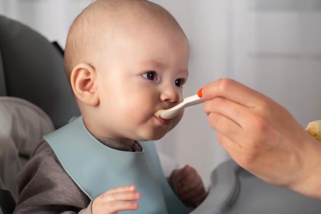 Woman feeds an eight-month-old baby solid foods. 