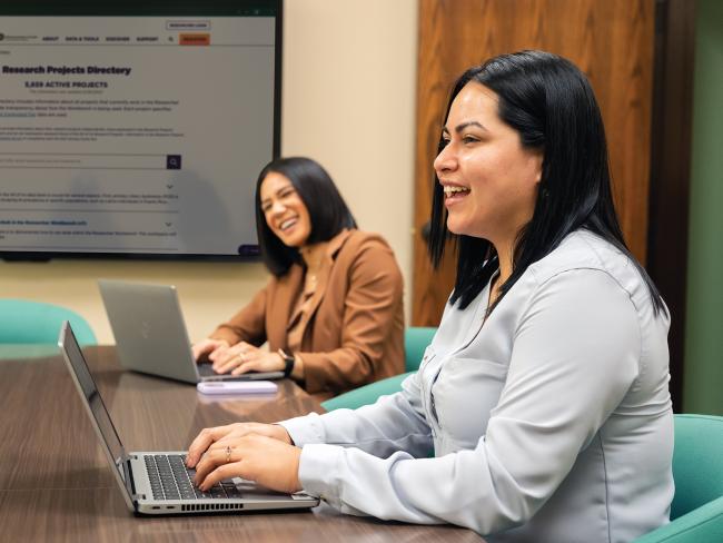 two women at laptops in a conference room