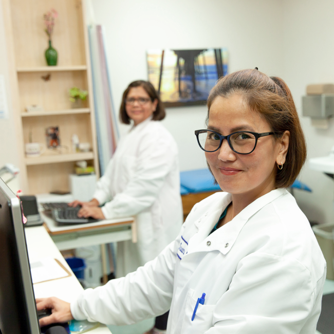 two women in lab coats at computer workstations in a clinical setting