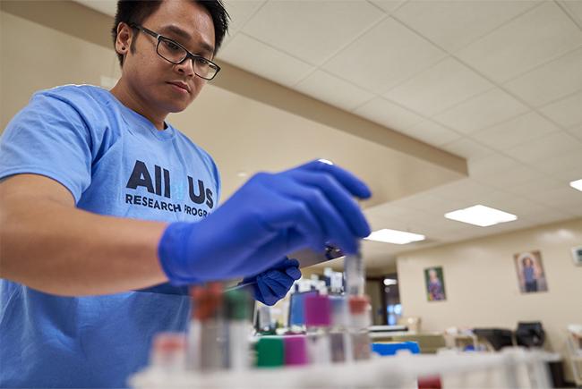 All of Us team member places a test tube into a rack alongside other biosamples in a lab setting