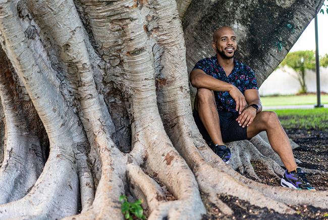 man sitting in a park, under or against a tree, in a bayfront setting