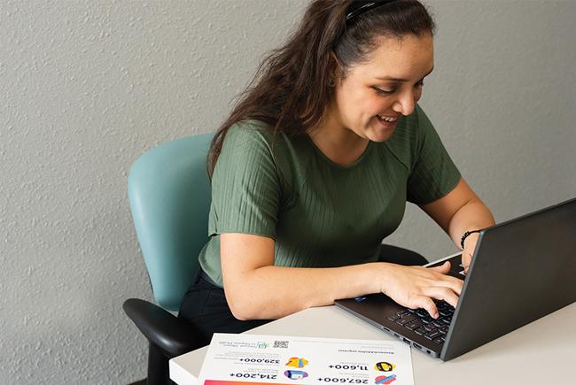 person at a desk, typing on a laptop