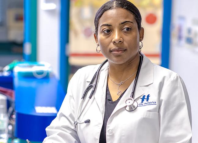 physician in white coat with stethoscope at desk