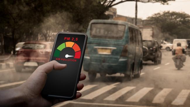 A person uses a smartphone app to measure air pollution in a hazy, traffic-heavy city. 