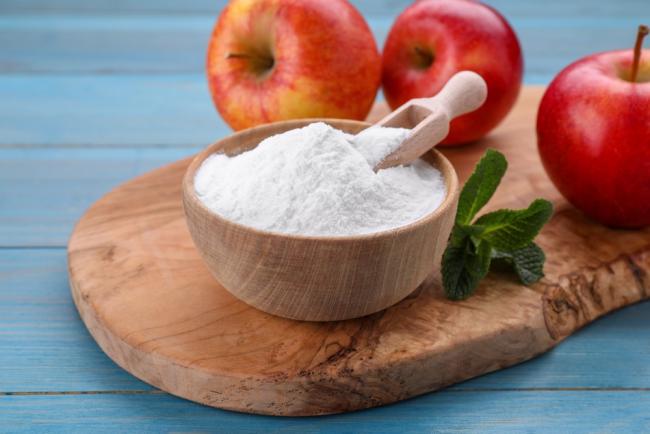 A bowl of fructose powder is surrounded by apples and mint sprigs.