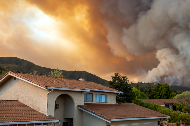 A home with thick wildfire smoke filling the sky in the background.