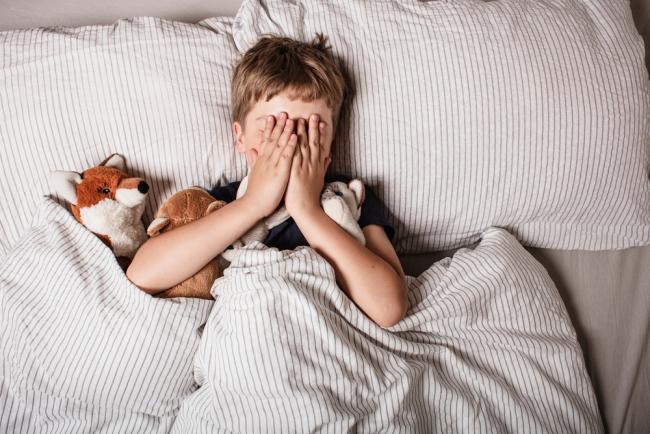 A young boy covers his face with his hands at bedtime. 