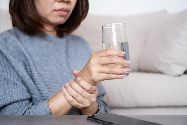 Woman holds a glass of water in one hand and uses her other hand to steady her movements. 