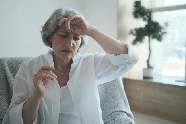 Middle-aged woman holds the back of her left hand to her forehead. 