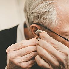 Older man places a hearing aid in his ear. 