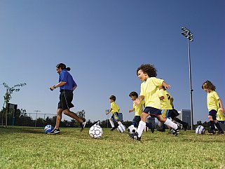Little league soccer team and coach practicing in park.