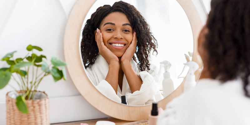 A young African American woman in a bathrobe, reflecting in mirror of a dresser table.