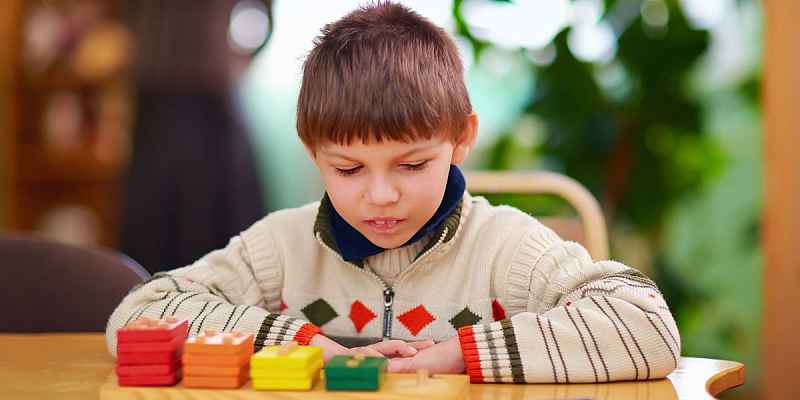 一个小男孩低头看了看成堆的木制方块，它们是按颜色和大小排列在一块钉板上的。