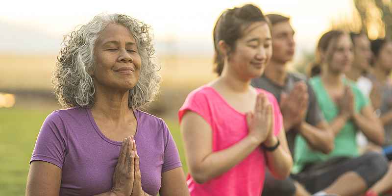 Older adult smiling and meditating during a group yoga class