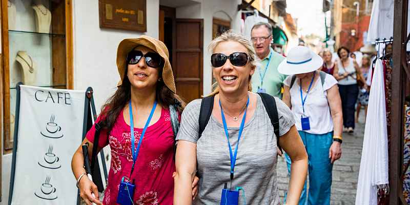 An adult with a visual impairment taking a group audio tour through a city while on vacation with a friend.