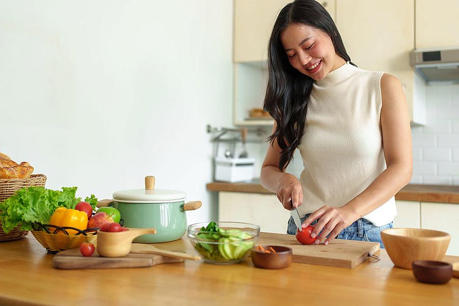 Woman cutting a tomato to make a salad in the kitchen.