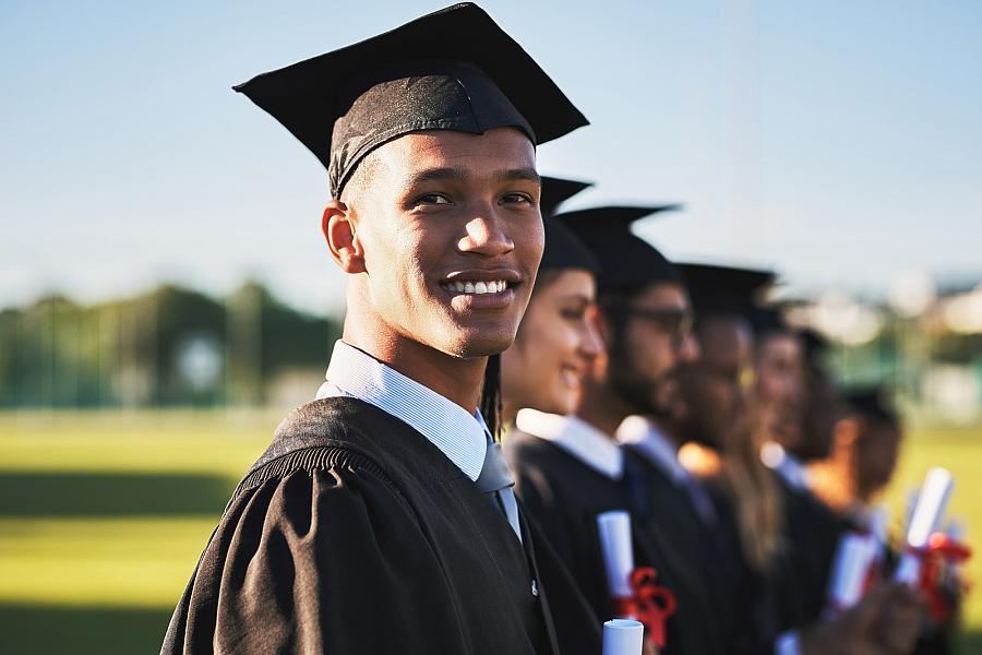 Smiling adults in graduate attire stand shoulder-to-shoulder.