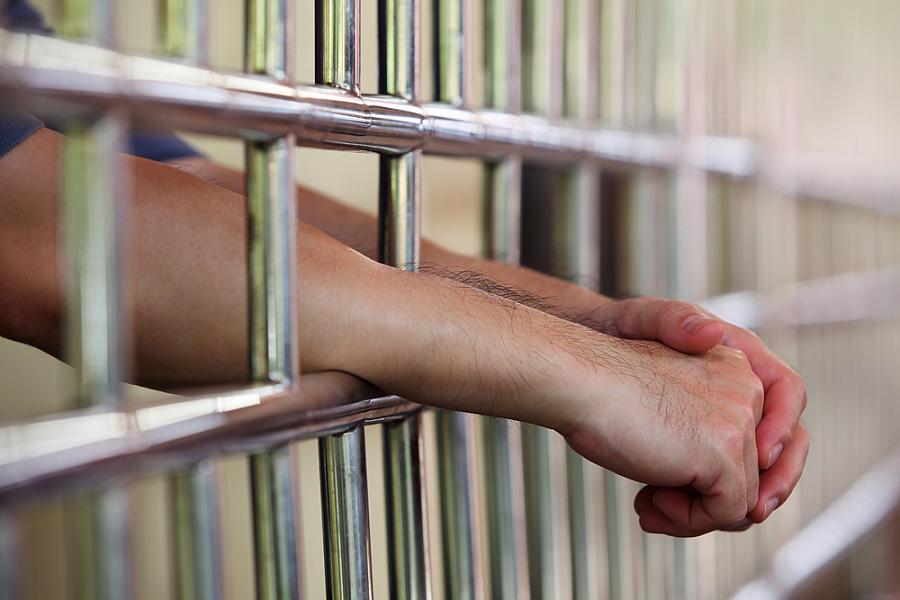 Clasped hands reaching out of a jail cell.