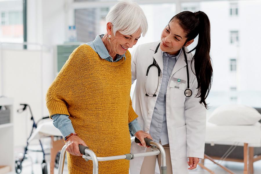 Doctor and elderly woman using a walker for support.