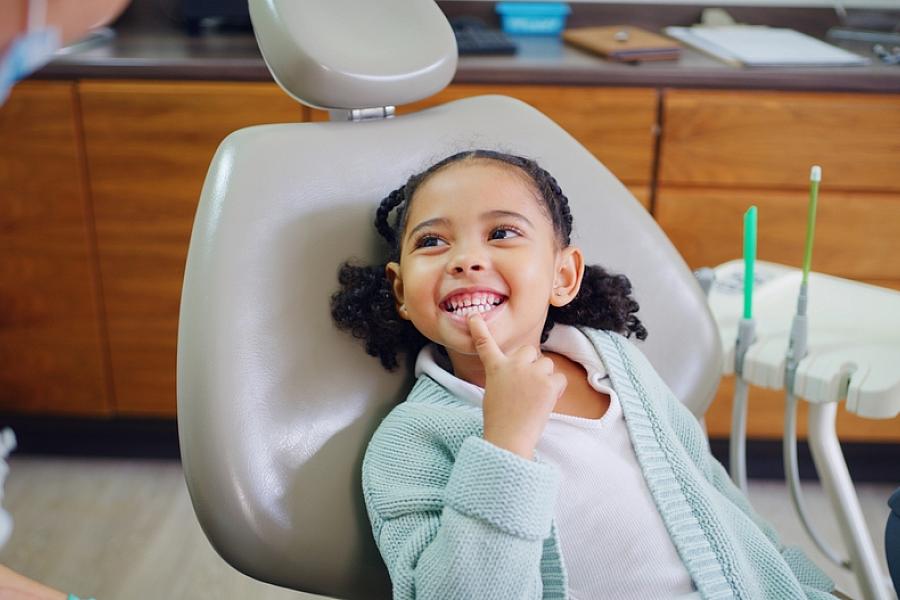 Young child smiles, pointing to her teeth, during dental checkup.