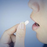 Photo of a woman taking a pill.