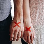 Two people’s hands marked with red X’s