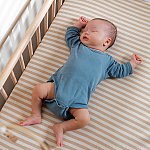 A baby sleeping on its back in an empty crib with a fitted sheet