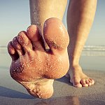  Bare feet walking on sand at the beach.