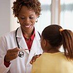 A doctor with a pleasant smile looks at the reading on a thermometer. Her hand is on the patient's shoulder.