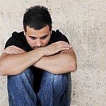 Depressed man sitting against a wall.