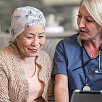 A female patient wearing a headscarf sits next to a female physician. The physician is showing the patient a wireless tablet.