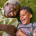 A senior man and his young grandson lying in the grass and laughing